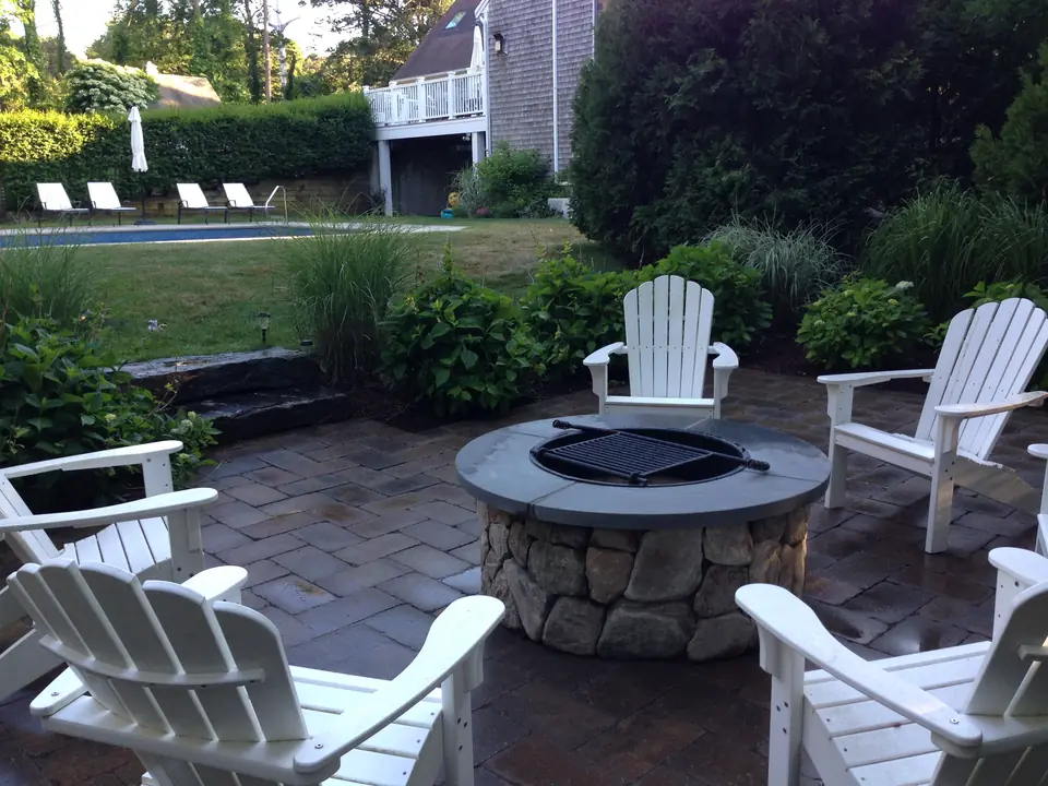 Fieldstone fire pit with a grate, on a paver patio beside the pool