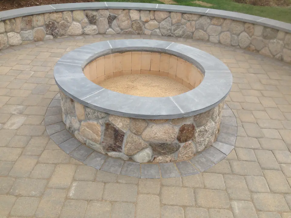 Fire pit with a bluestone cap in front of a fieldstone seat wall