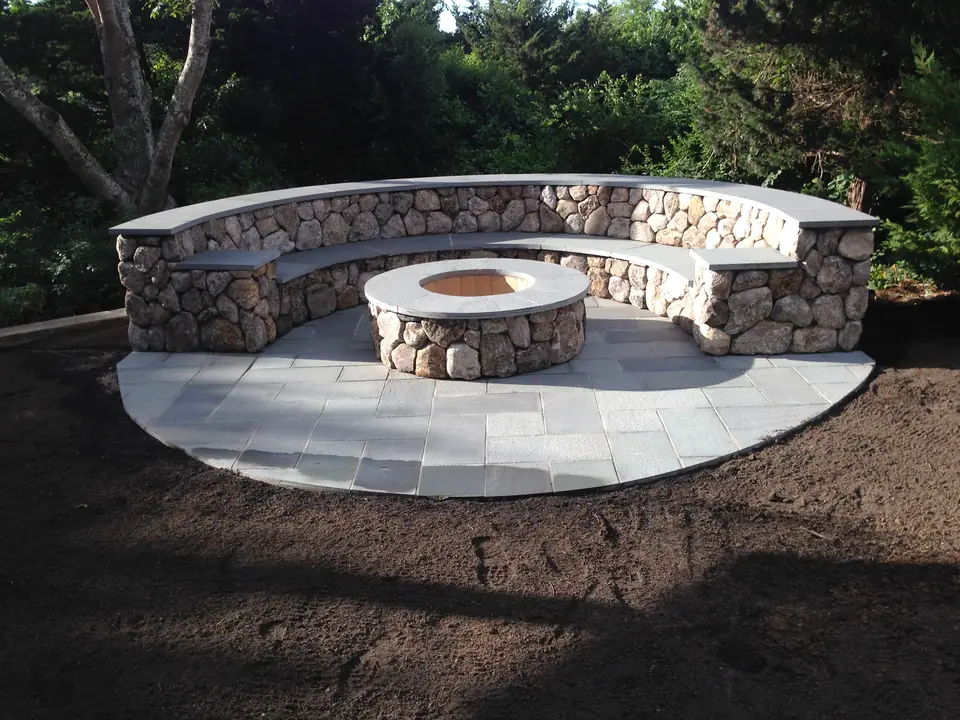 Curved fieldstone seat wall and fire pit on a bluestone pad, at dusk