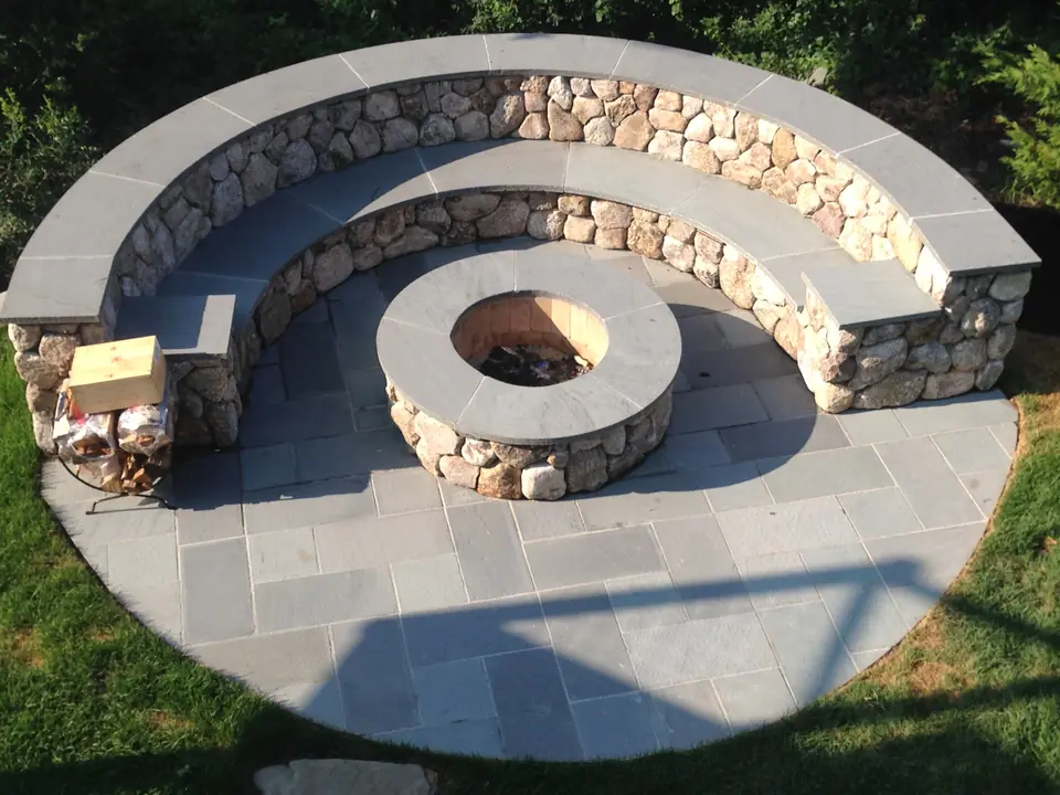 Two-tier fieldstone seat wall and fire pit with bluestone caps, on a round bluestone patio