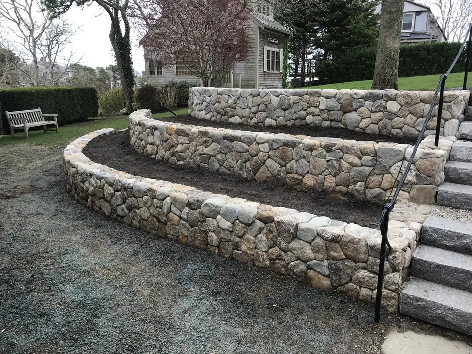 Two curved fieldstone retaining walls with granite steps and a railing